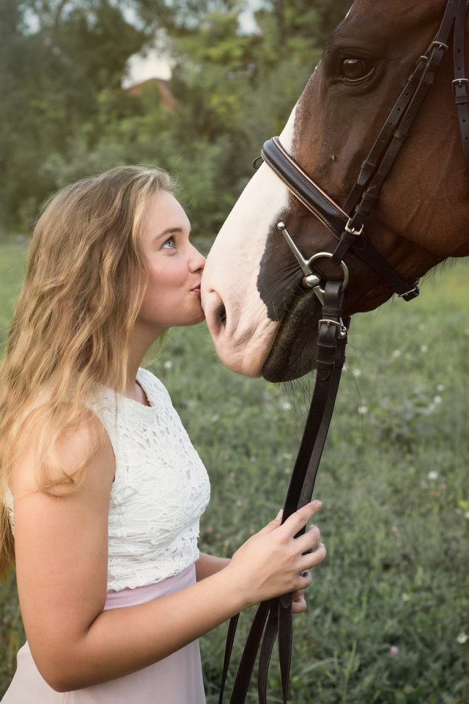 girl kissing white nose of bay horse