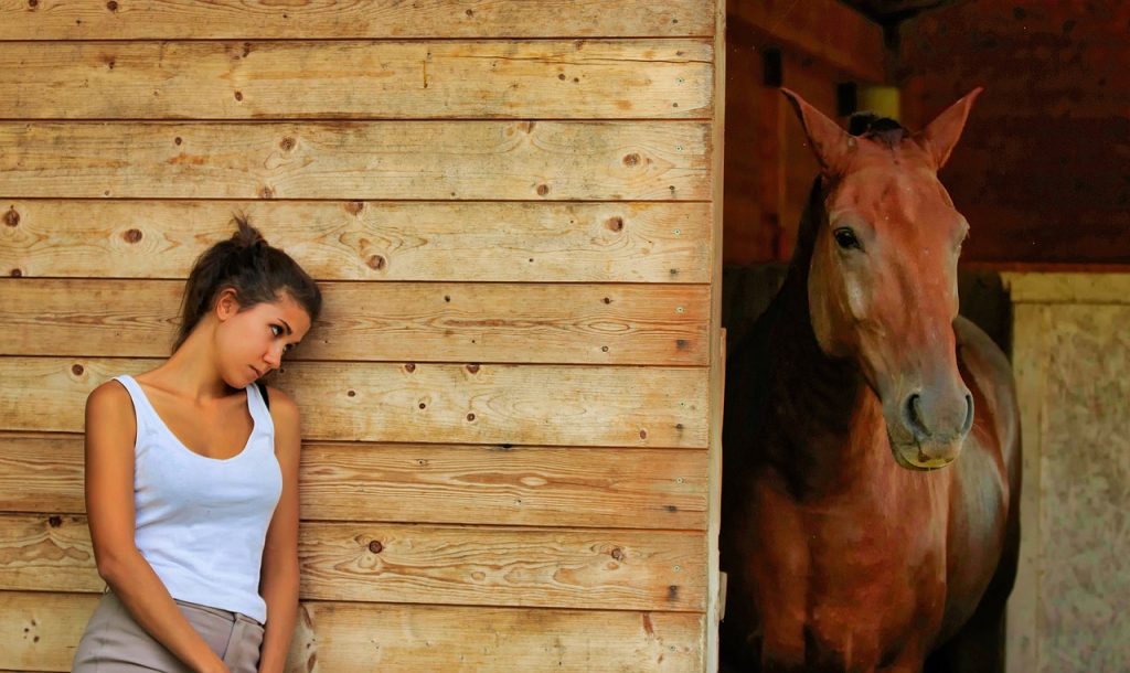 girl looking sad outside horses stall while horse looks out of stall doorway